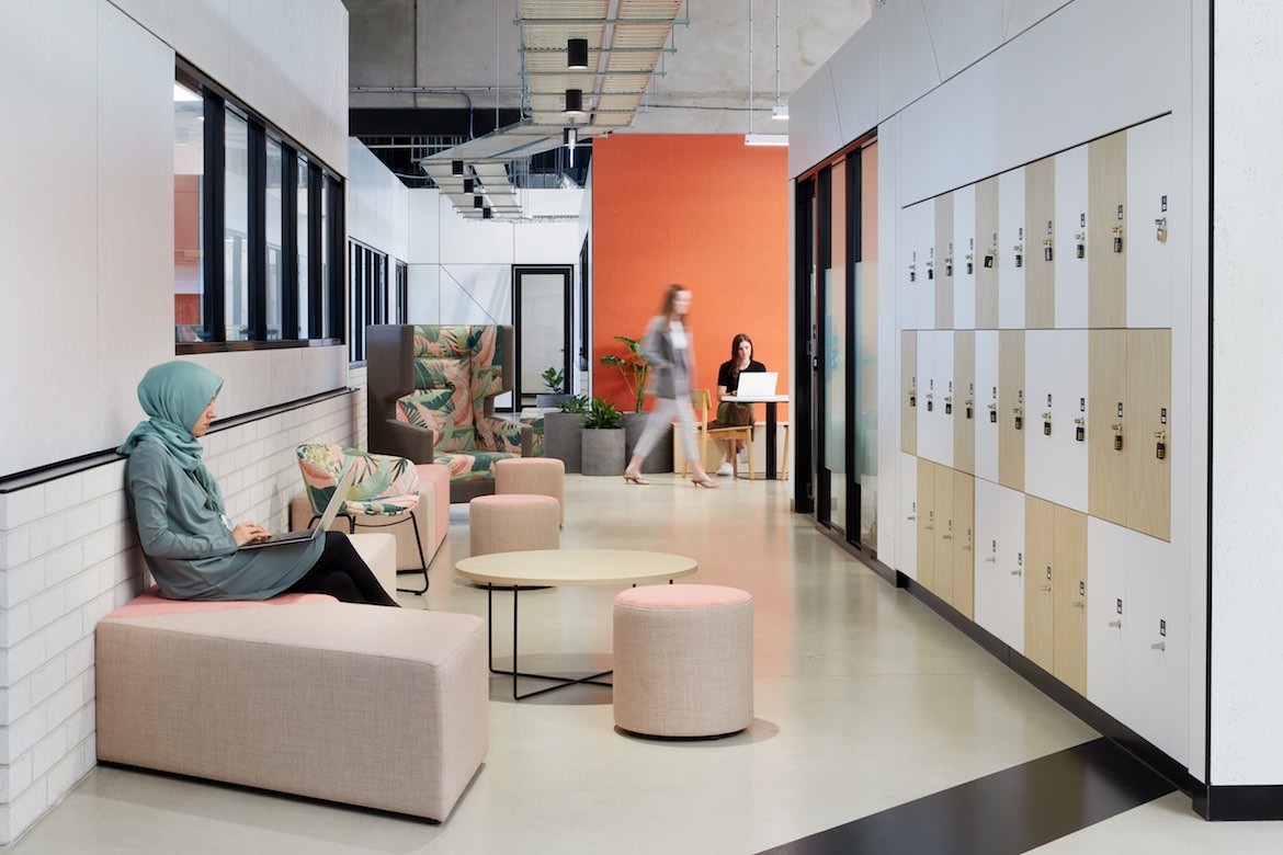 A person wearing teal sits using a laptop in a corridor across from lockers in Hester Hornbrook Academy by Gray Puksand.