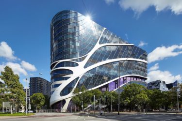 A large sculptural curved glass and steel building by DesignInc with blue sky behind.