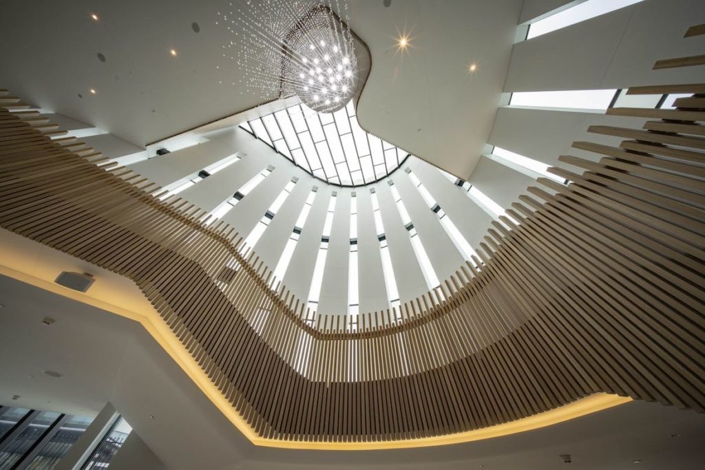 Looking up at the Field of Stars Chandelier in the high ceilinged atrium of Sydney Coliseum Theatre with the wood panelling railing of the sweeping staircase nearby.