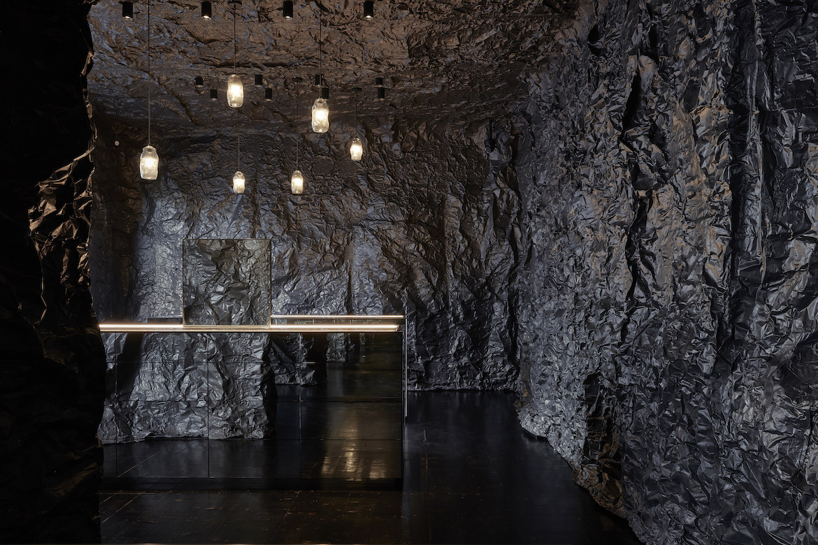 A retail space with black undulating walls, mirrored display cases and low lighting.