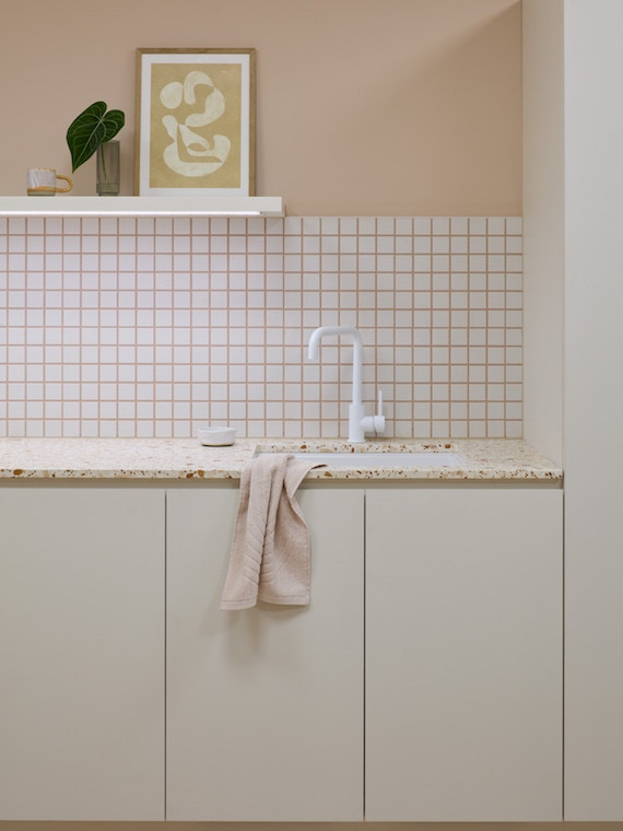 A grid of cream tiles with dusty pink grouting behind the apricot terrazzo bench in the tea area of New Me medical centre by Rezen Studio.