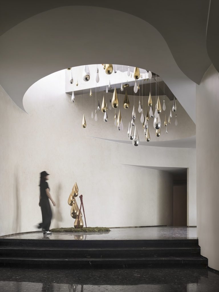 A woman walks past dripping pendant sculptures and curving walls in The future ark sales centre.