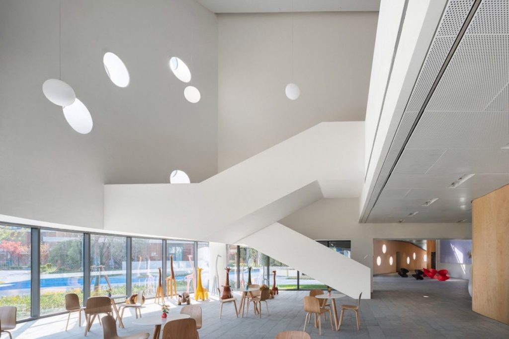 A white staircase and high ceiling in Pinghe Bibliotheater with a range of wooden chairs and tables in the foreground.