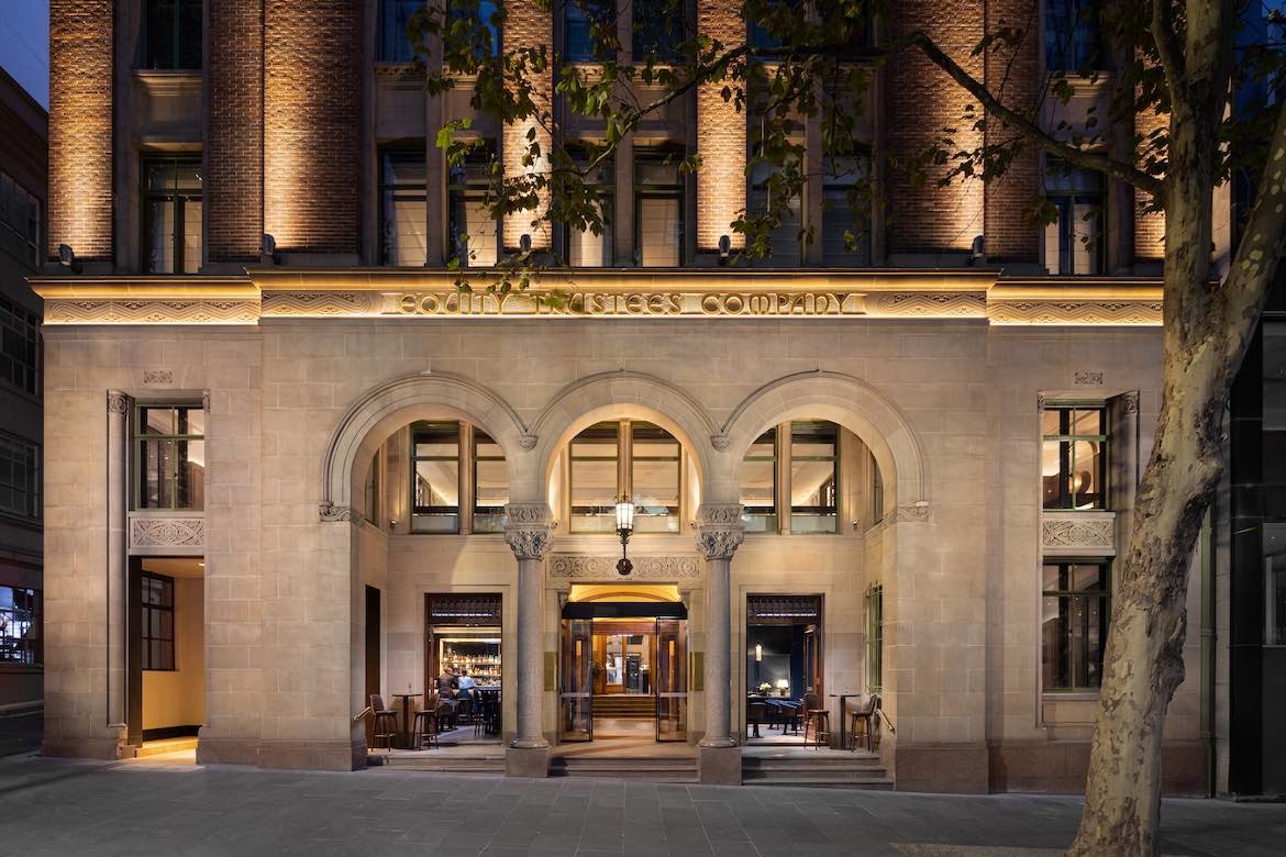 The lower section of the exterior facade of the Hilton Melbourne Little Queen Street, with text reading Equity Trustees Company above a large triple-arched entrance.