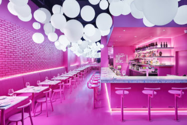 The pink interior of Ping Pong, with a bar lined with pink powder-coated derlot stools and tables lining the other wall.