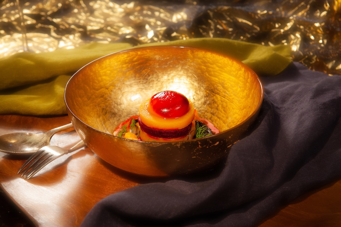 A gold bowl of food next to a fork and spoon, by Bompas & Parr at Expo 2020