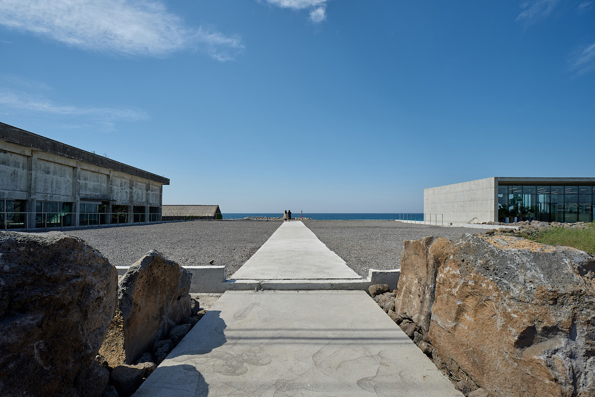 A pathway between the concrete buildings of Gongbech, towards the water.