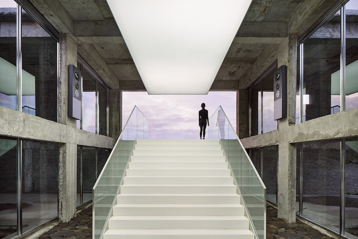 A white staircase in Gongbech leading up to an exit with a person standing looking out towards purple dusk clouds.