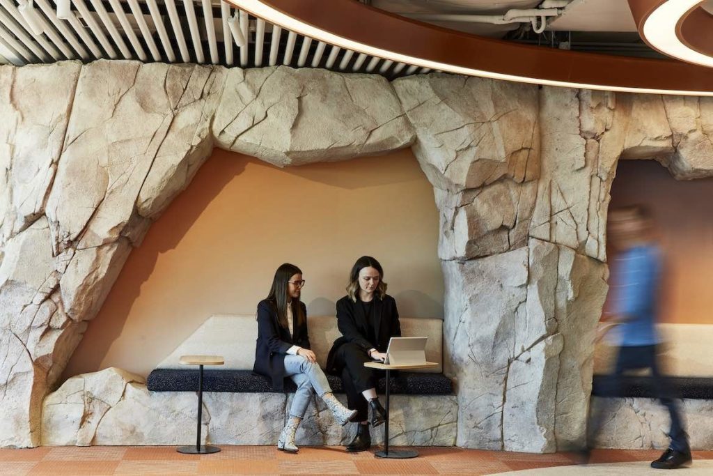 Two women sit in a bench seat embedded in a rock wall in the Microsoft Sydney headquarters designed by group GSA.