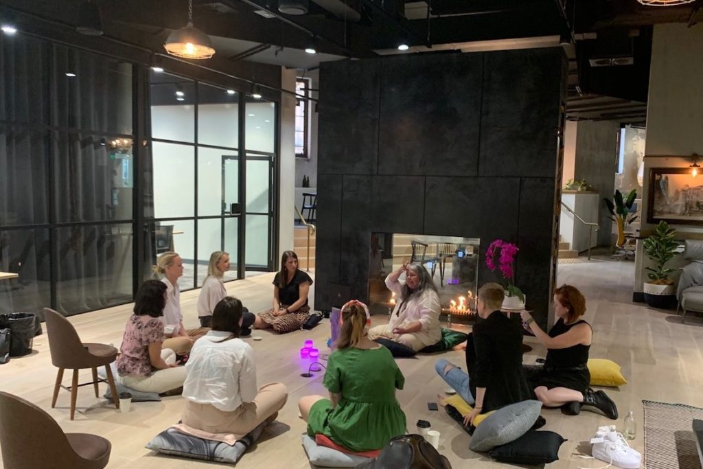 Susan Moylan-Coombs sits with a group of people on cushions on the floor in a Haworth wellbeing circle.