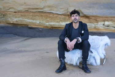 Léo Terrando sits in front of a rock wall on a beach.