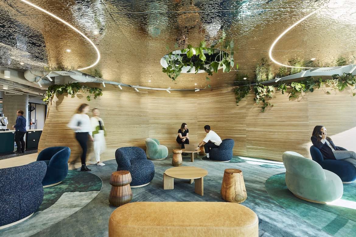 People sit in squat blue and green armchairs on a turquoise carpet, under a reflective gold roof with plants hanging from the ceiling in the Microsoft Sydney headquarters designed by group GSA.