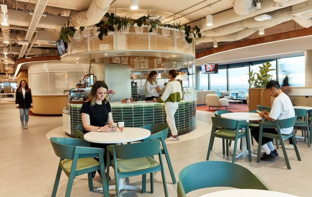 People sit in green chairs around small round white tables in the cafe area of the Microsoft Sydney headquarters designed by group GSA.