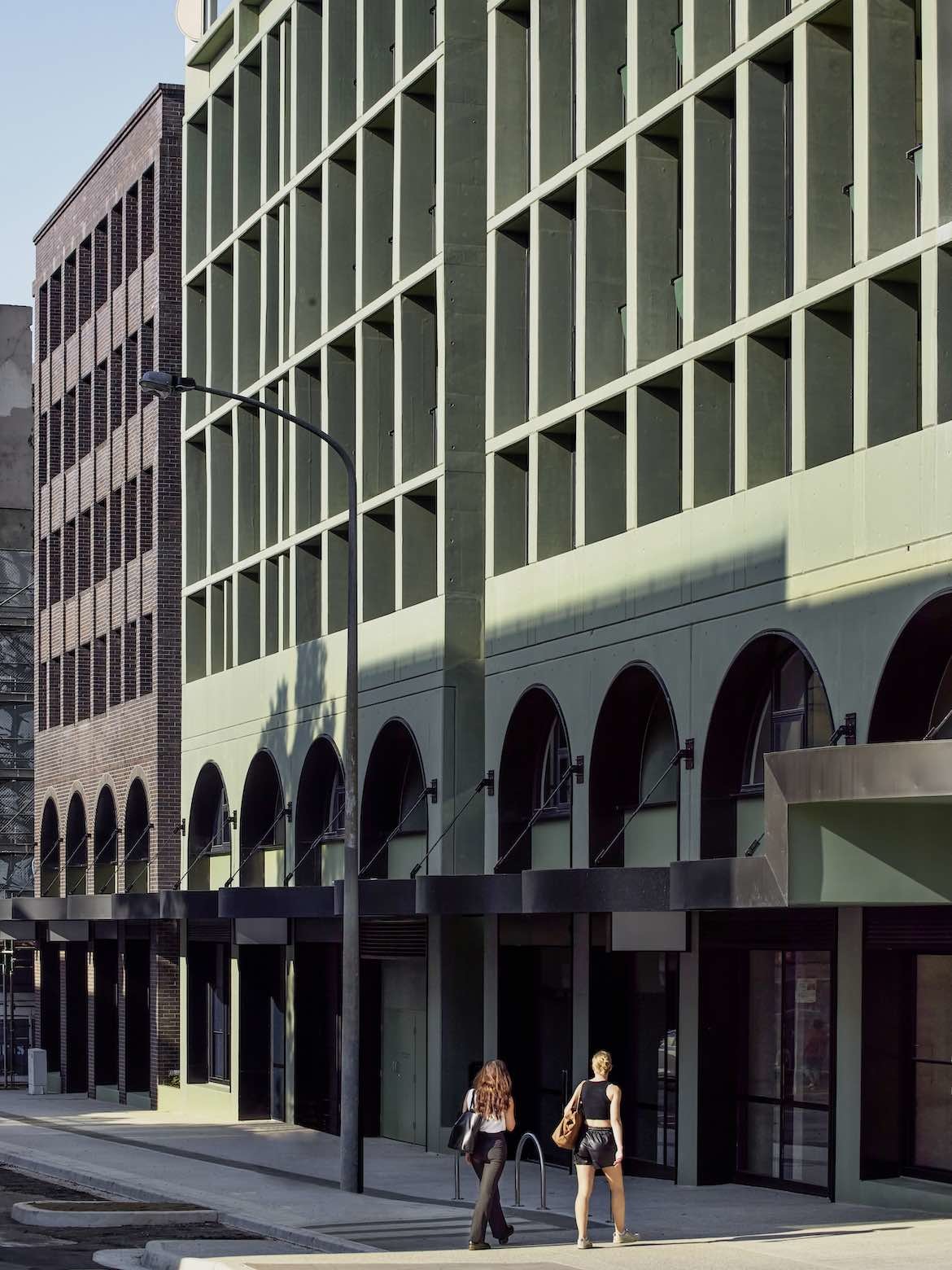 The sage-green exterior of Newcastle East End mixed-use development with large arches, designed by SJB.
