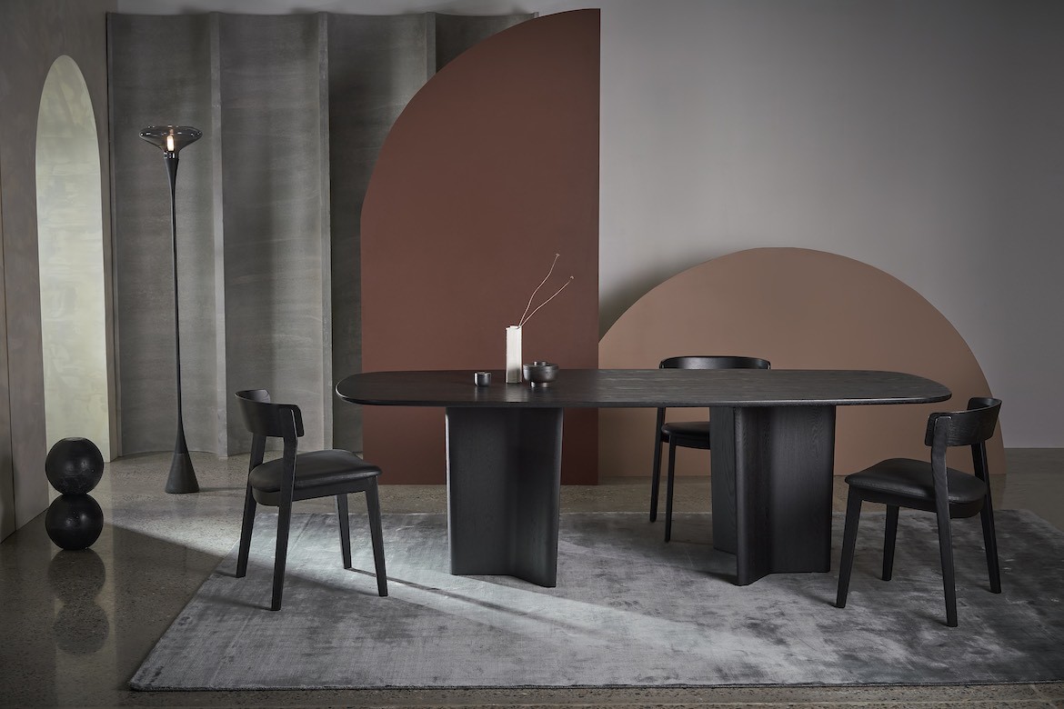 A black table on a grey rug, in front of beige and tan background shapes.