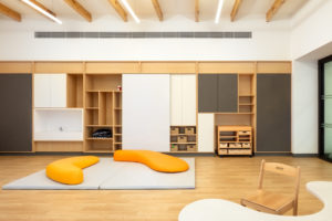 Curved orange seating areas and a curved grey table in a classroom with pale floors, white walls and wooden beams in The Heritage School.