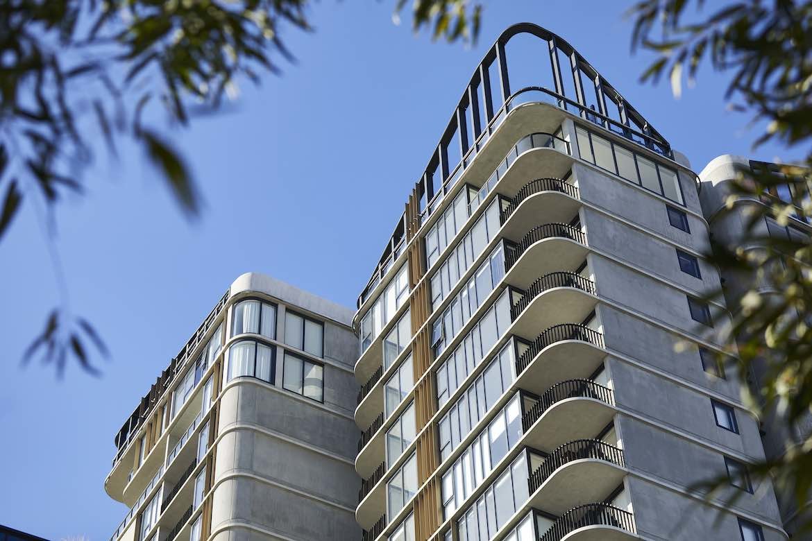 The tall exterior of Waterfall by Crown group, displaying rounded edges, concrete, greenery and wood panelling.