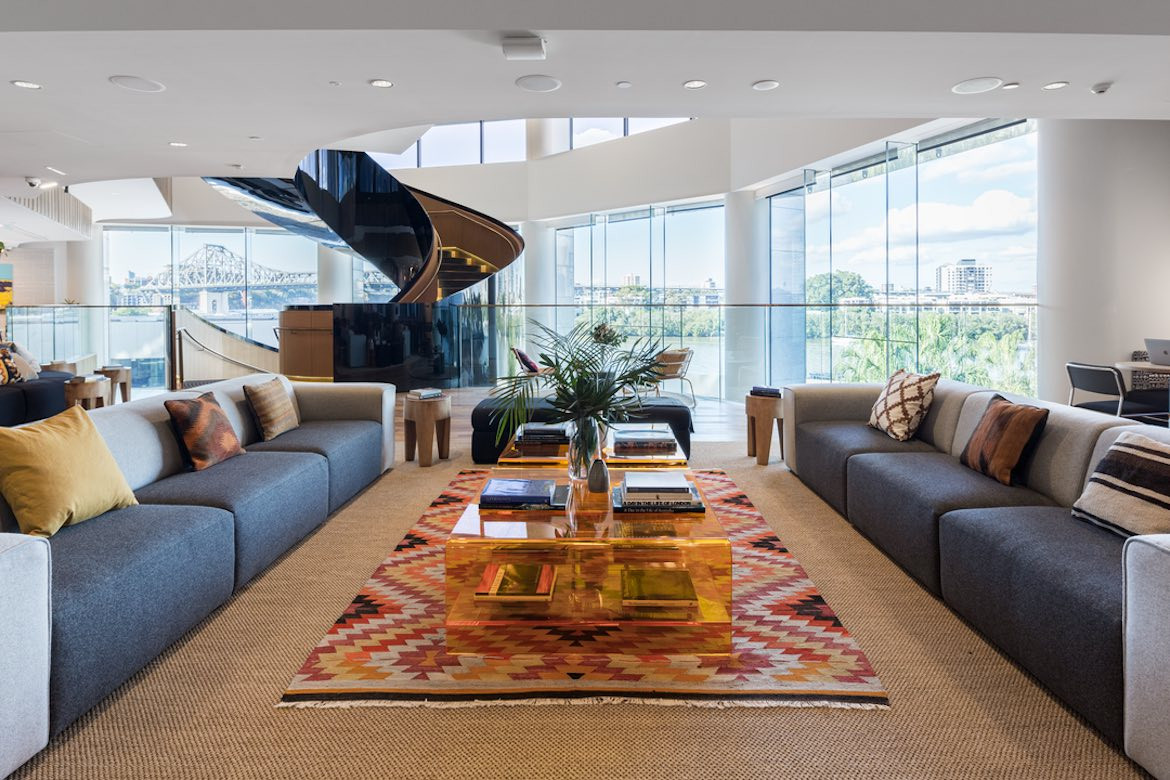 A WeWork lounge area with beige carpet, a red rug and a large black spiral staircase in the background.