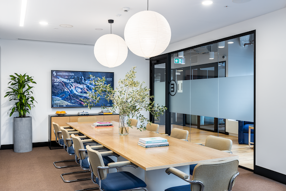 A long office conference table surrounded by blue chairs in a WeWork meeting room.