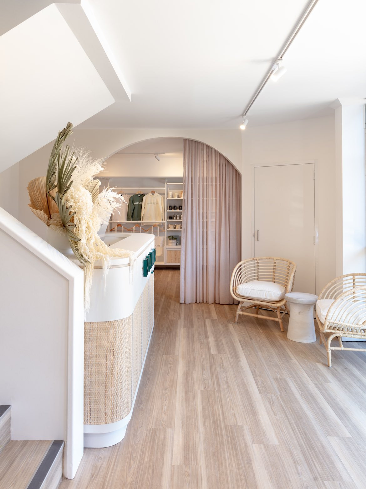 Two cane armchairs and a small table sit across from the curved white reception desk, near an arched doorway in Holixir by Building Guild.