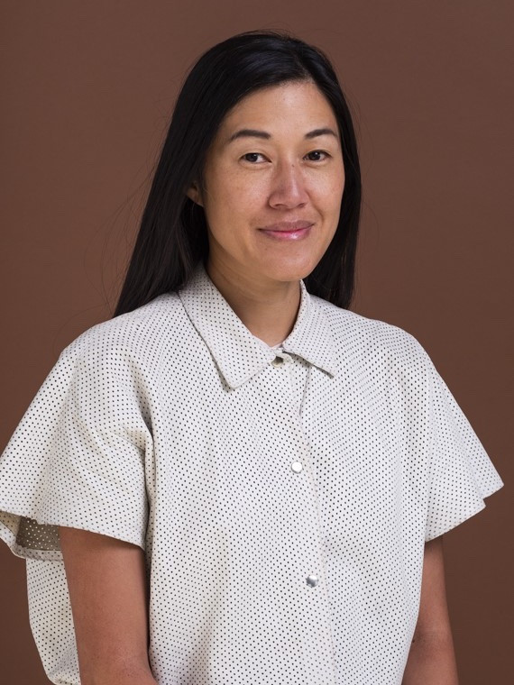 Qianyi Lim, a research of New Agency, wears a white t-shirt and sits in front of a brown background.